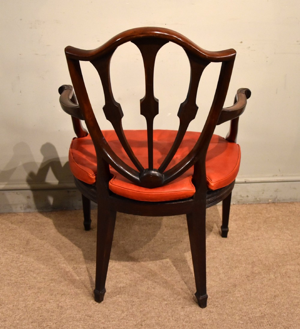 An 18th-century George III carved mahogany armchair featuring a shield-shaped open backrest, swept armrests, and a button-tufted red leather seat cushion. View V