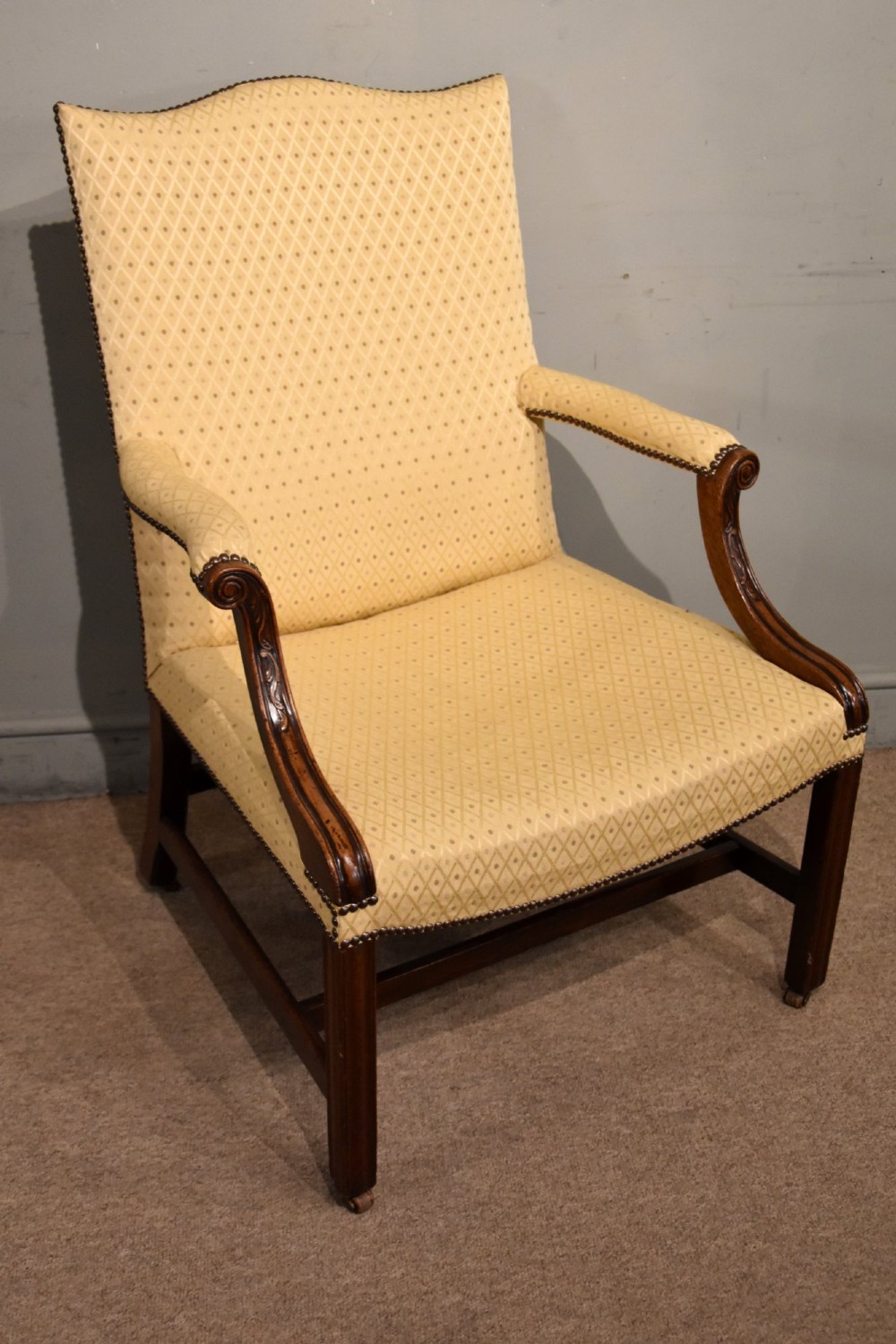 A George III mahogany Gainsborough library armchair upholstered in yellow patterned fabric with scroll arms and brass stud trim. View II