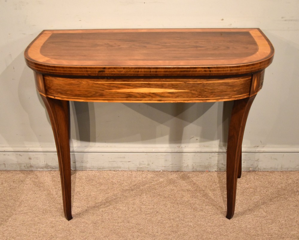 A Regency rosewood foldover card table featuring satinwood crossbanding and an inlaid diamond motif on swept legs.