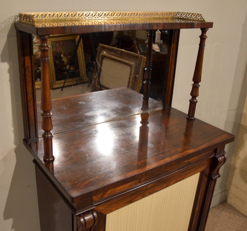 A George IV rosewood chiffonier featuring a raised mirrored back shelf with turned columns and a top brass gallery, set above a lower cupboard door with a pleated cream fabric panel. View V