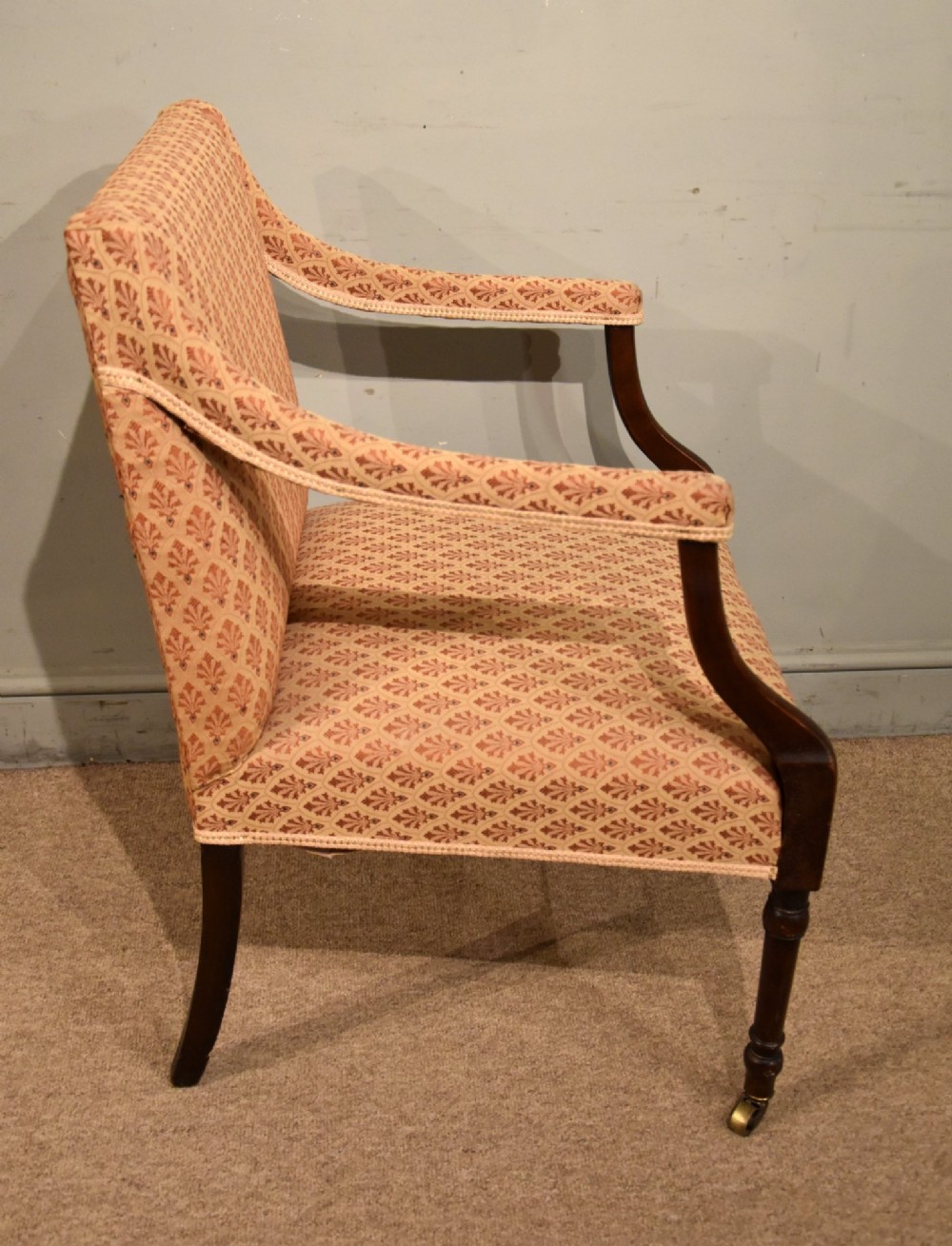 A pair of antique mahogany armchairs featuring terracotta pattern upholstery, sweeping armrests, turned front legs, and brass castors. View V