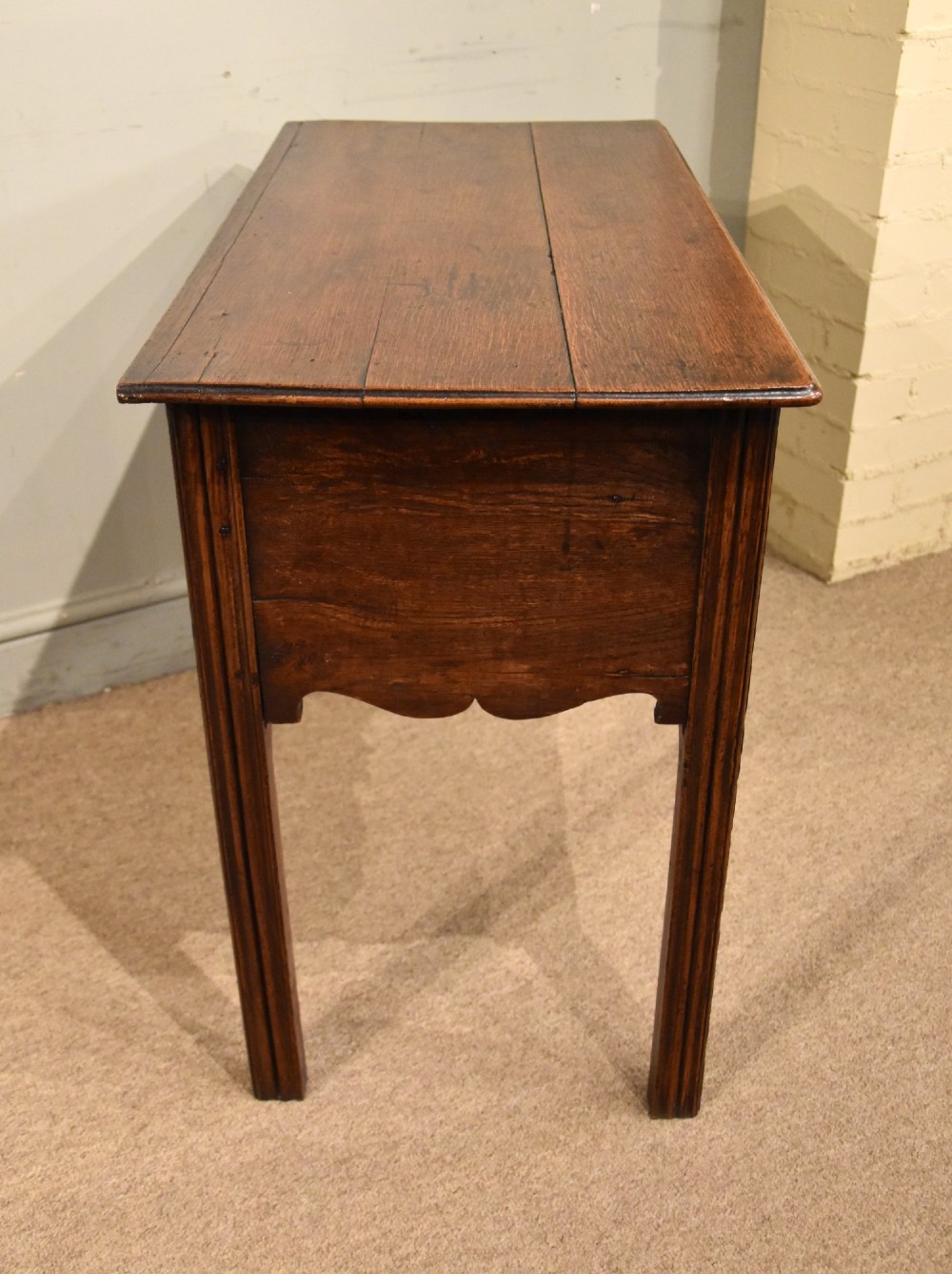 A George III oak lowboy side table featuring one wide upper drawer above two smaller drawers, fitted with brass swan-neck handles, a scalloped apron, and reeded square legs. View VI