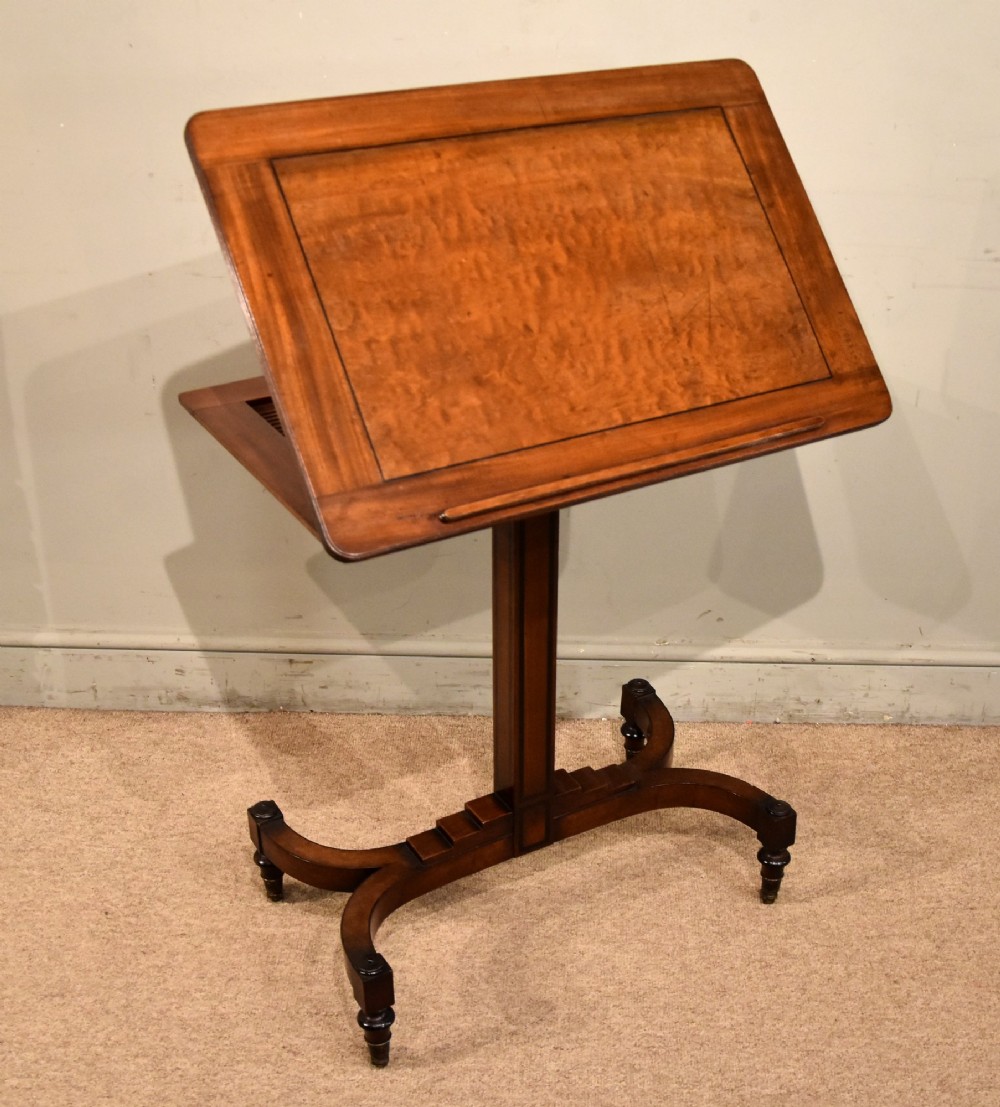 A Regency period mahogany reading stand featuring a rectangular tilting top resting on a central pedestal column with splayed legs and brass castors. View VI
