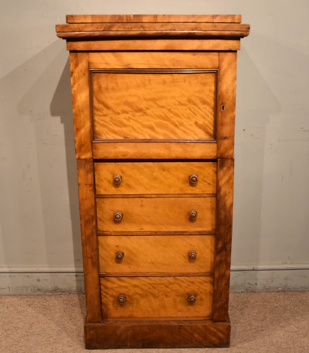 A tall Victorian satin birch Wellington chest featuring multiple drawers, a top secretaire compartment, turned wooden knobs, and a hinged side locking bar on a plinth base. View II