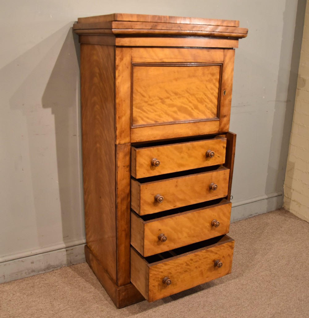 A tall Victorian satin birch Wellington chest featuring multiple drawers, a top secretaire compartment, turned wooden knobs, and a hinged side locking bar on a plinth base. View III