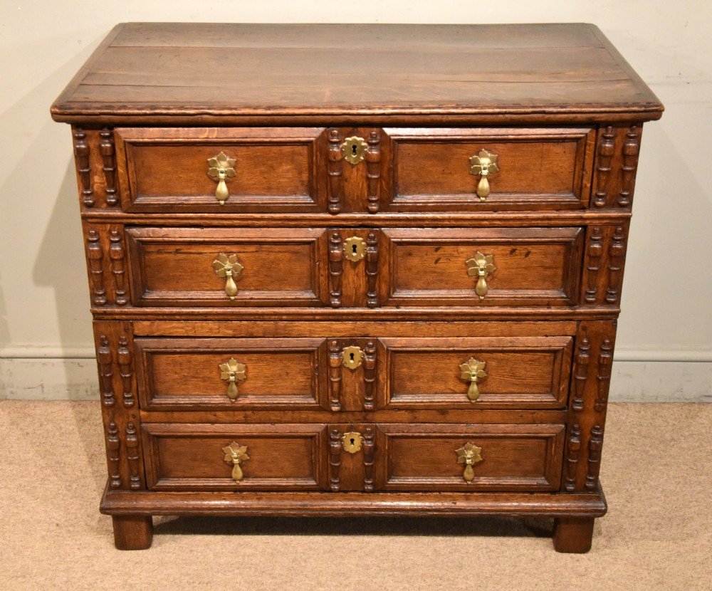 A Charles II oak chest of drawers featuring geometric panelled drawer fronts, split-baluster mouldings, brass drop handles, and escutcheons. View II