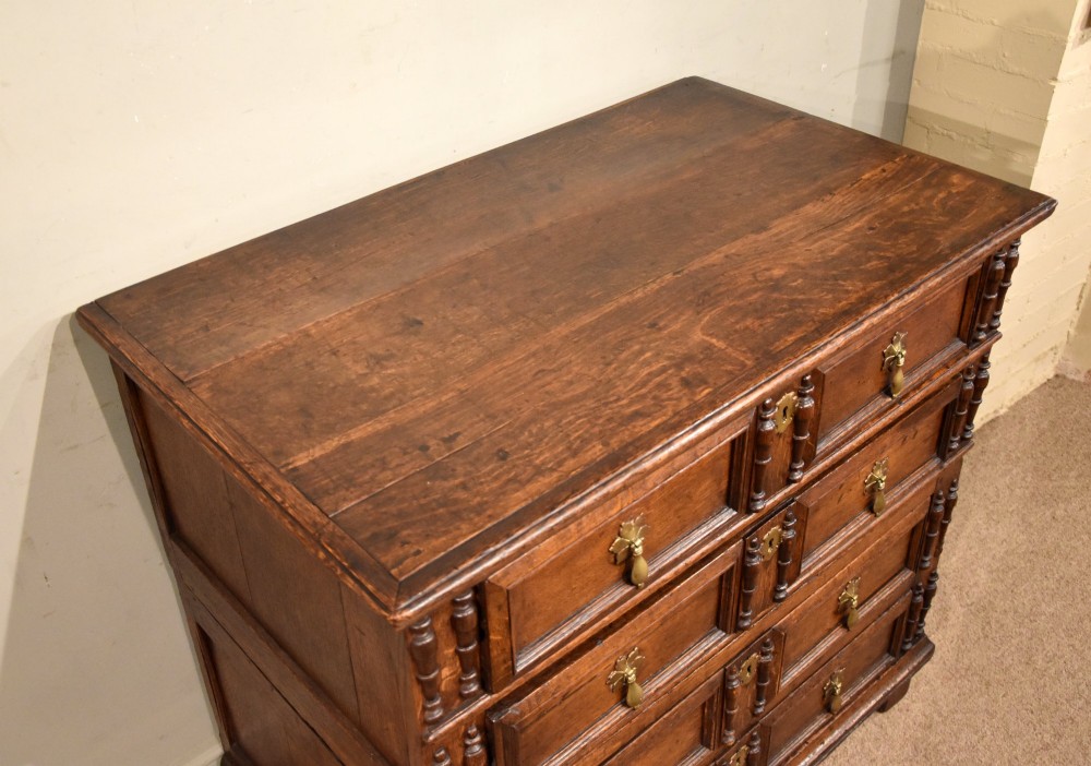 A Charles II oak chest of drawers featuring geometric panelled drawer fronts, split-baluster mouldings, brass drop handles, and escutcheons. View V