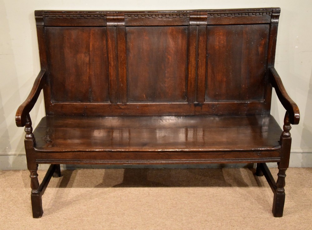 An 18th century dark oak settle bench featuring a three-panelled high backrest, curved armrests, and turned front legs. View II