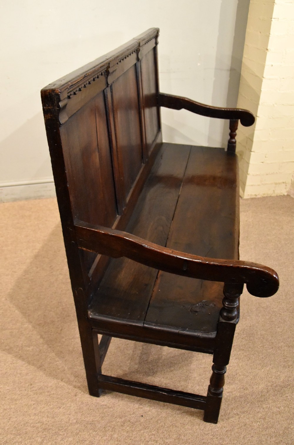 An 18th century dark oak settle bench featuring a three-panelled high backrest, curved armrests, and turned front legs. View V
