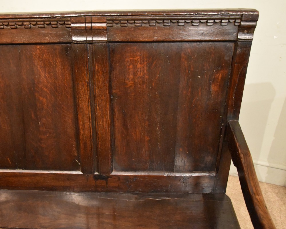 An 18th century dark oak settle bench featuring a three-panelled high backrest, curved armrests, and turned front legs. View VI