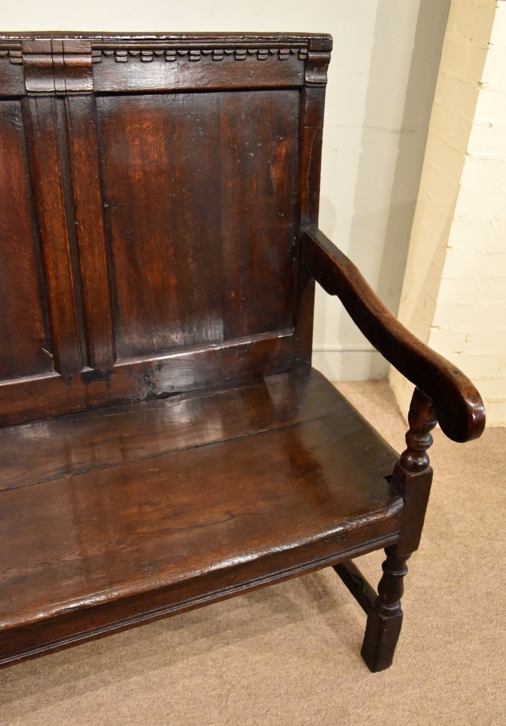 An 18th century dark oak settle bench featuring a three-panelled high backrest, curved armrests, and turned front legs. View VII