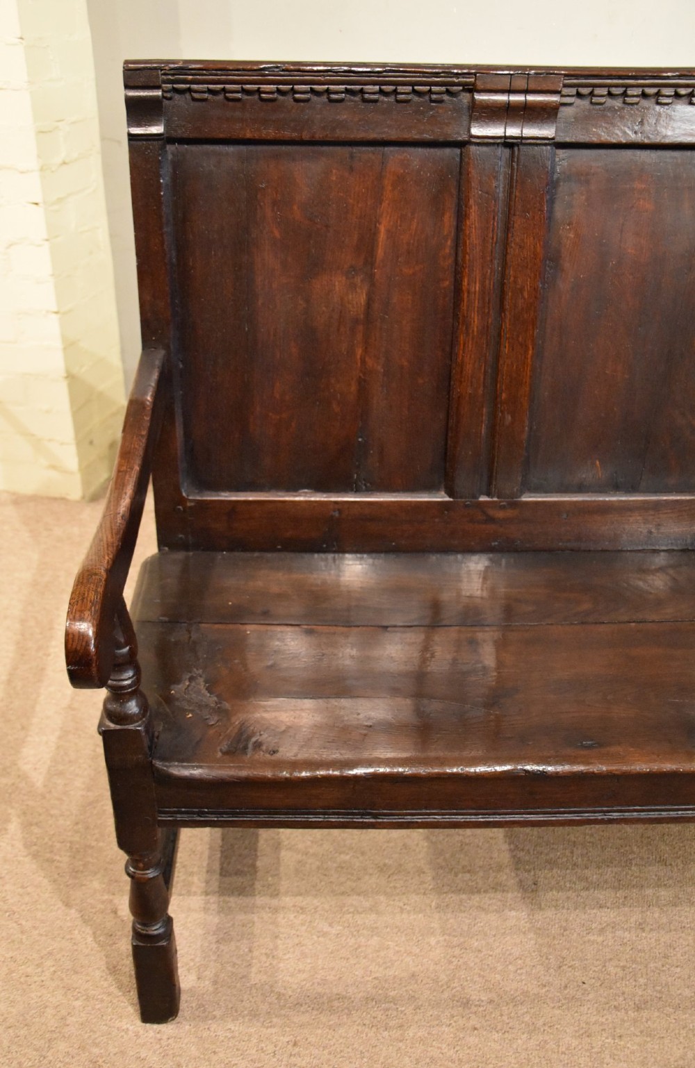 An 18th century dark oak settle bench featuring a three-panelled high backrest, curved armrests, and turned front legs. View VIII