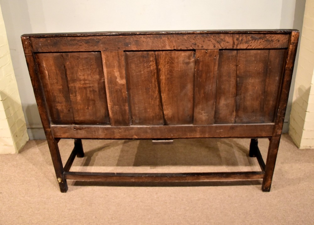 An 18th century dark oak settle bench featuring a three-panelled high backrest, curved armrests, and turned front legs. View IX