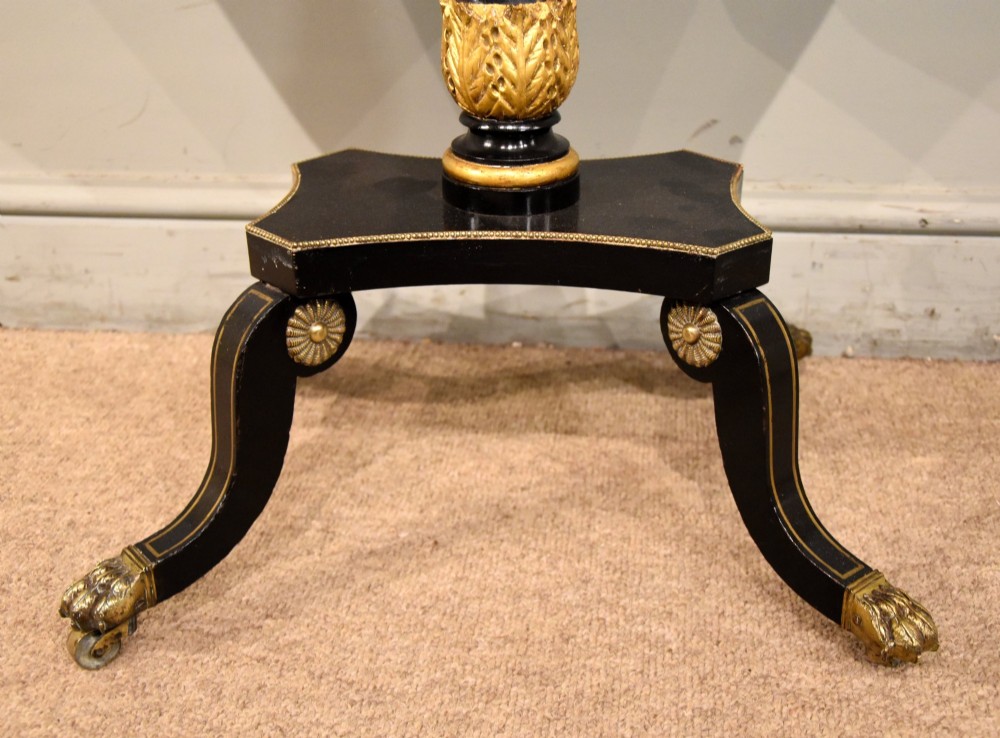 A Regency ebonised and gilt octagonal sewing table featuring detailed penwork on the lid, a pleated cream fabric basket beneath, and a central column resting on swept legs with brass castors. View VIII