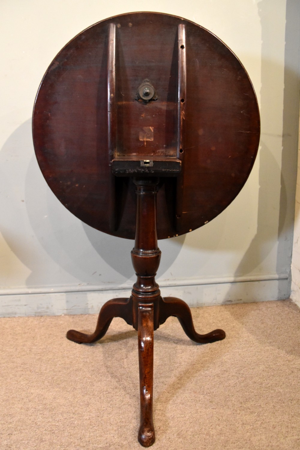 A George III mahogany tilt-top tripod table shown with its circular top tilted vertically on a turned stem and cabriole legs. View III