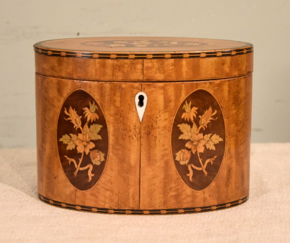 An 18th-century oval satinwood tea caddy featuring floral marquetry inlays, decorative stringing, and a bone keyhole escutcheon. View VI