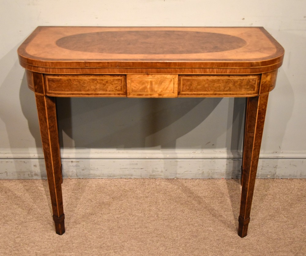 A George III fold-over card table with burr yew wood veneer, an oval central inlay, and square tapered legs.