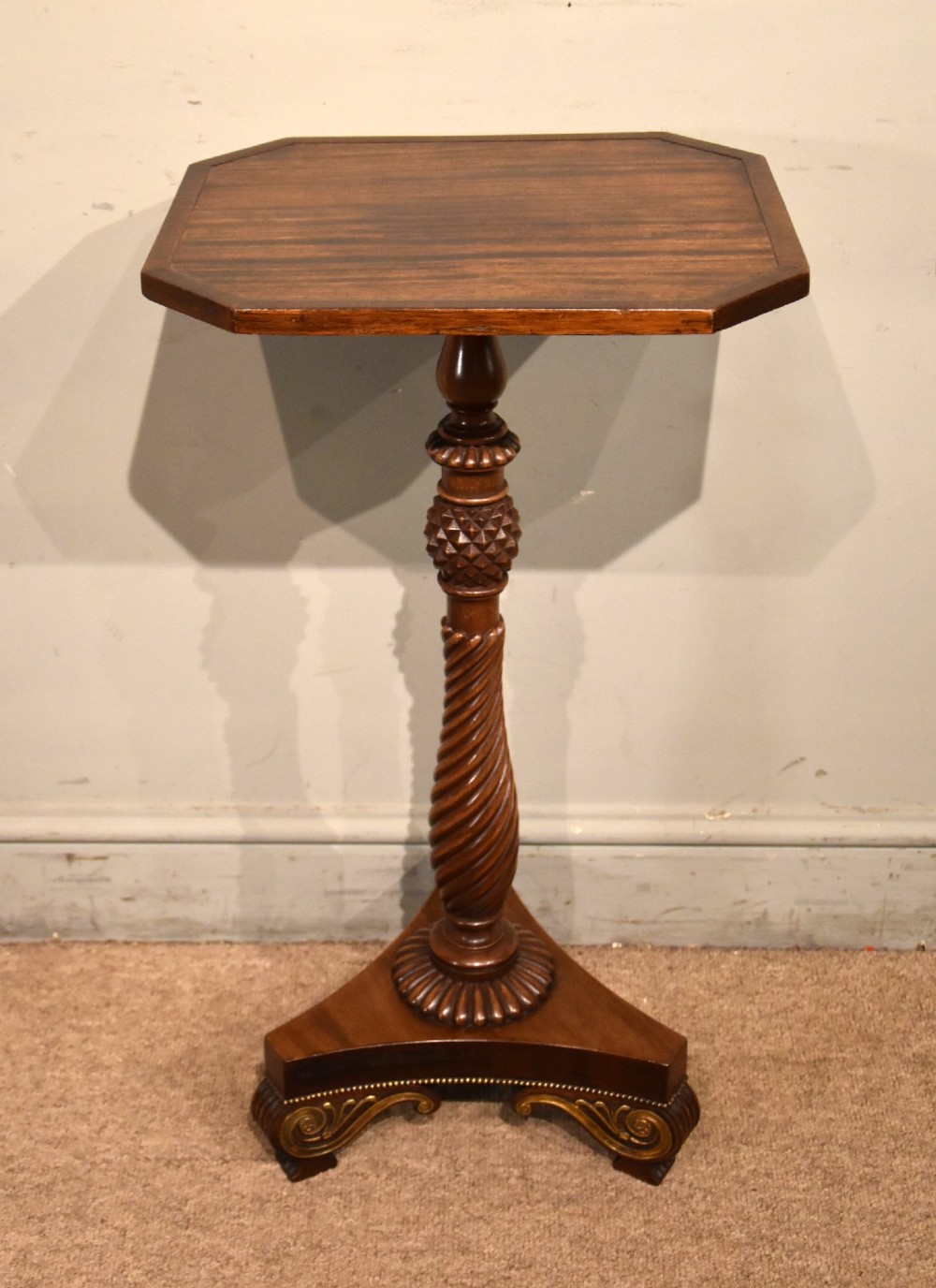 A Regency mahogany occasional table featuring an octagonal top, a carved spiral stem, and a tri-form pedestal base with scroll feet.