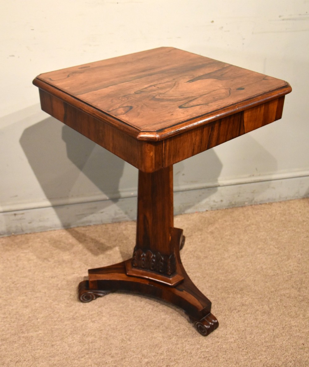 A William IV rosewood side table with a square top, plain frieze, tapered central pedestal, and a tri-form platform base on scroll feet.