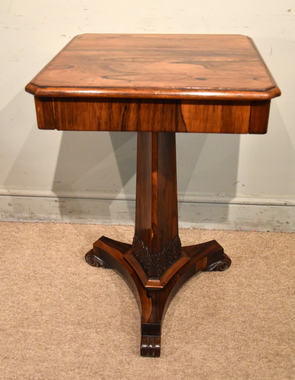 A William IV rosewood side table with a square top, plain frieze, tapered central pedestal, and a tri-form platform base on scroll feet. View II