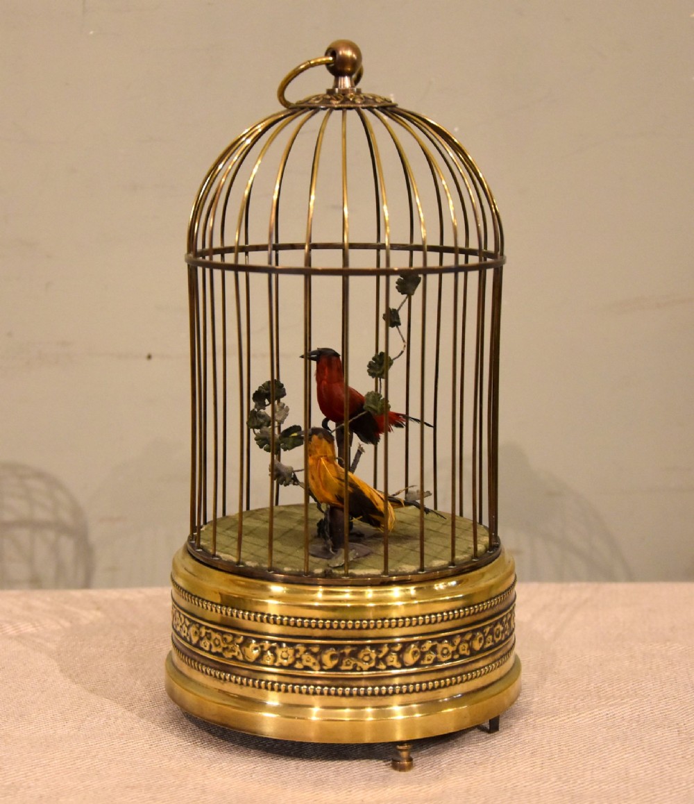 A Victorian brass birdcage automaton featuring two artificial feathered birds perched inside a domed wire cage over an embossed brass base.