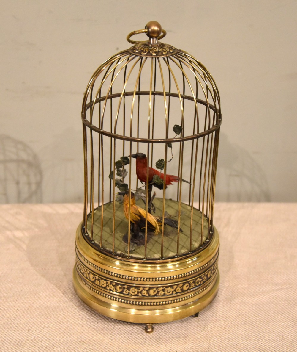 A Victorian brass birdcage automaton featuring two artificial feathered birds perched inside a domed wire cage over an embossed brass base. View II
