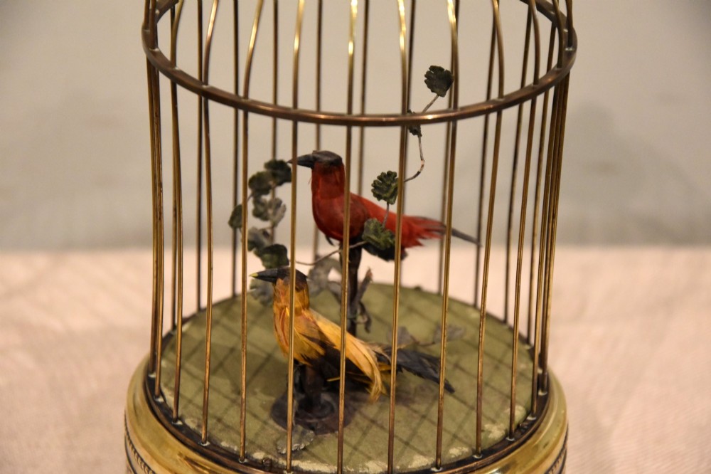 A Victorian brass birdcage automaton featuring two artificial feathered birds perched inside a domed wire cage over an embossed brass base. View IV
