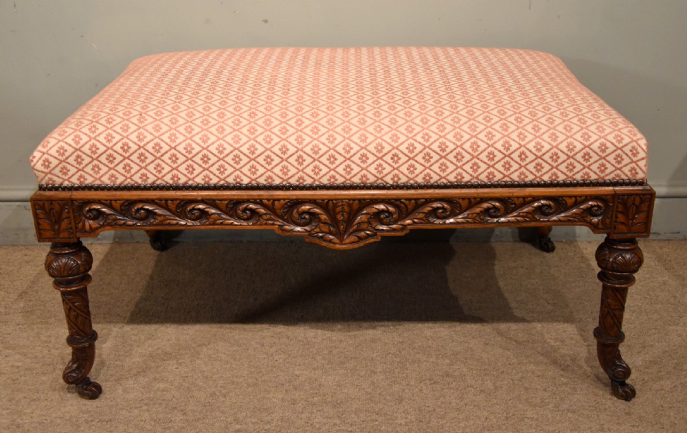 A Victorian rectangular rosewood dressing stool with patterned pink fabric upholstery, studding details, an acanthus-carved apron, and turned legs.