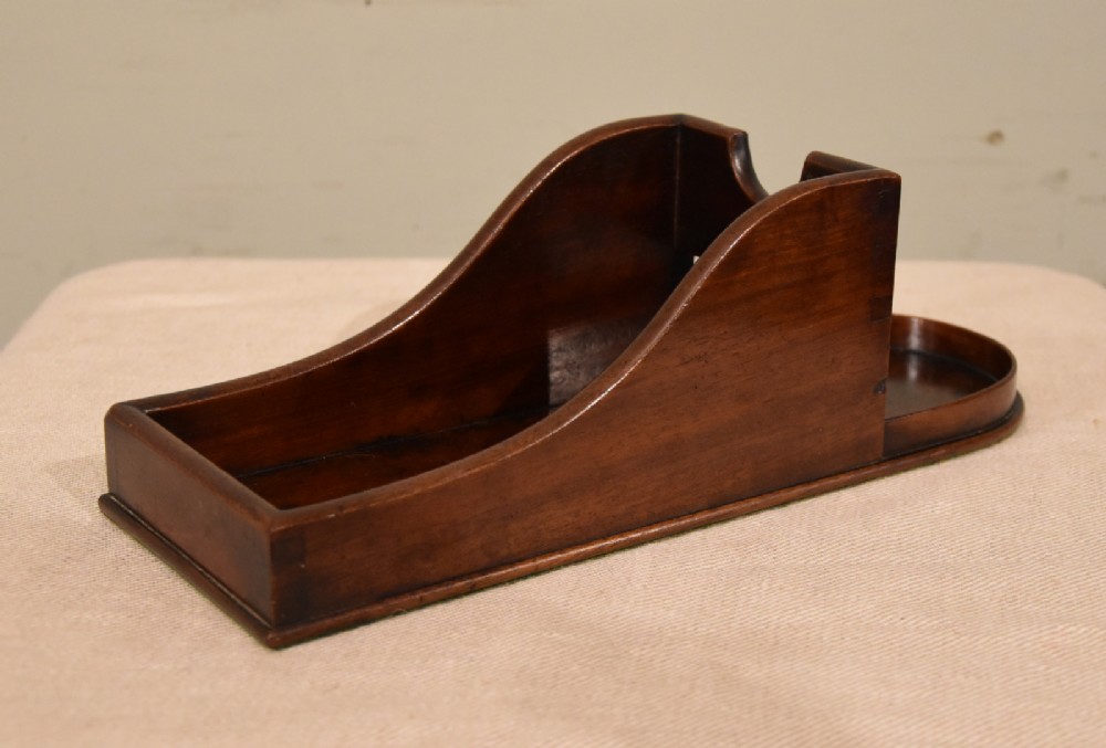 An antique Georgian mahogany wine bottle holder featuring carved swooping side panels and a recessed base.