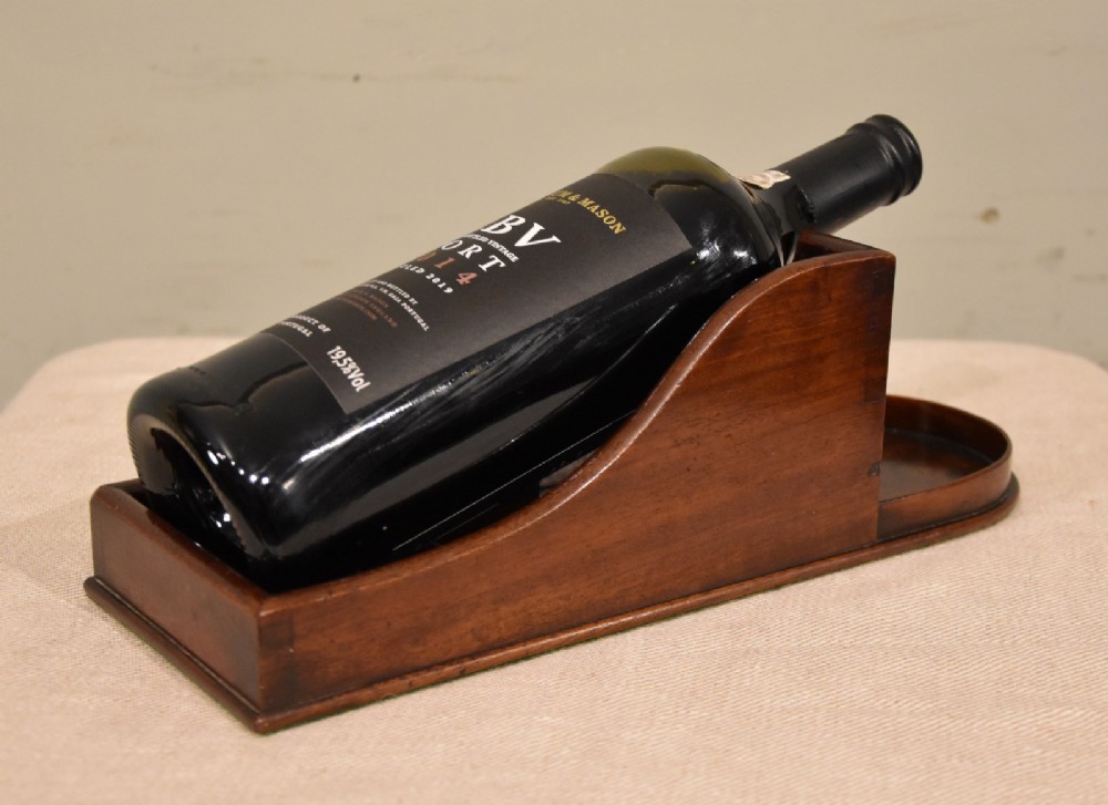 An antique Georgian mahogany wine bottle holder featuring carved swooping side panels and a recessed base. View II