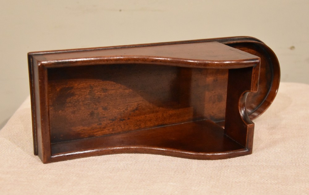 An antique Georgian mahogany wine bottle holder featuring carved swooping side panels and a recessed base. View III