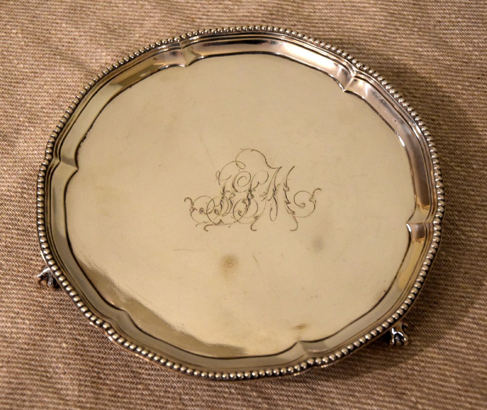 A circular Georgian sterling silver waiter featuring a beaded rim, central engraved monogram, and cast claw-and-ball feet. View II