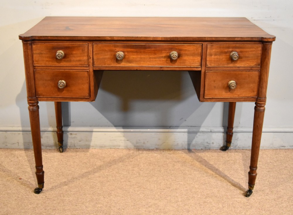 A Regency period mahogany dressing table featuring five drawers, circular brass handles, and turned tapered legs on brass castors.