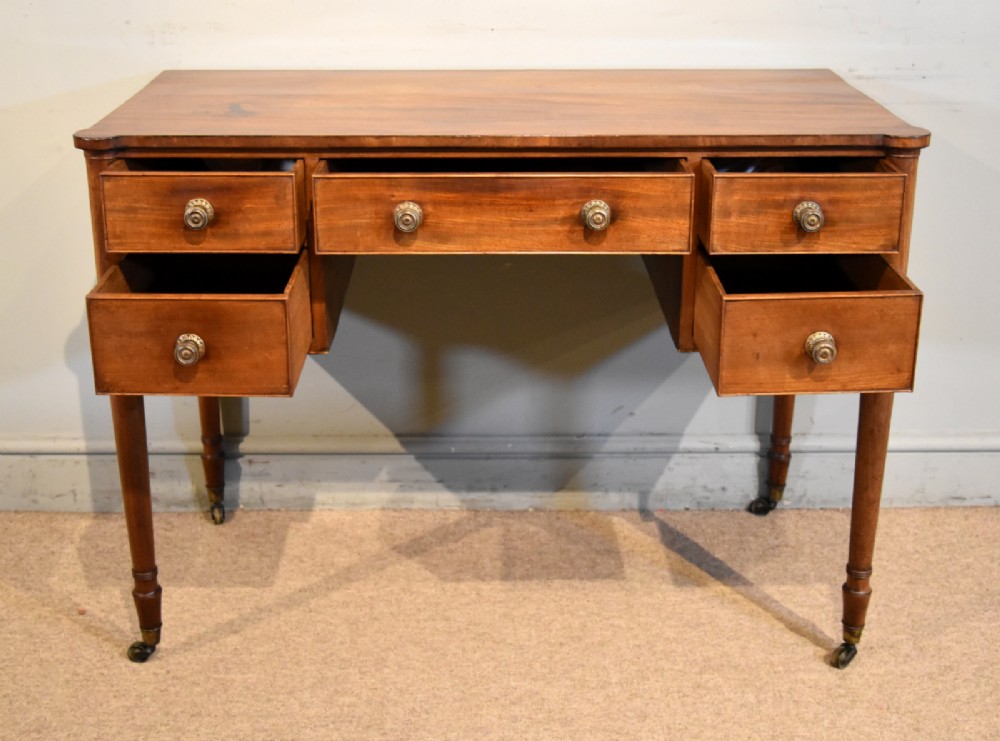 A Regency period mahogany dressing table featuring five drawers, circular brass handles, and turned tapered legs on brass castors. View II