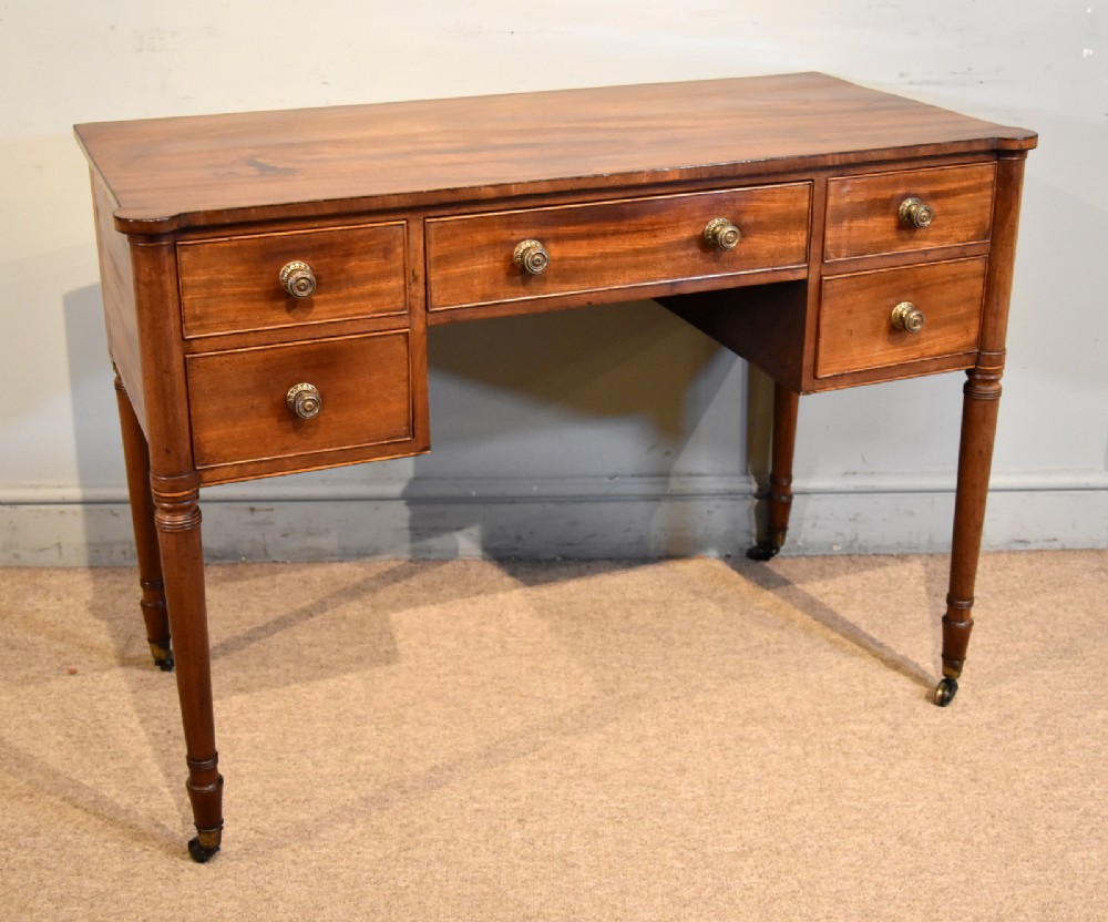A Regency period mahogany dressing table featuring five drawers, circular brass handles, and turned tapered legs on brass castors. View III