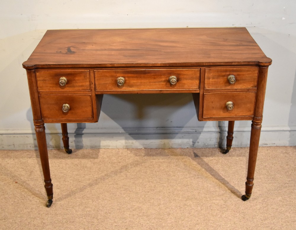 A Regency period mahogany dressing table featuring five drawers, circular brass handles, and turned tapered legs on brass castors. View IV