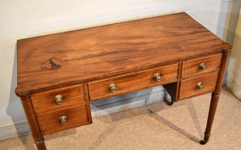 A Regency period mahogany dressing table featuring five drawers, circular brass handles, and turned tapered legs on brass castors. View V