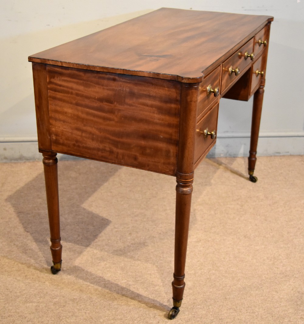 A Regency period mahogany dressing table featuring five drawers, circular brass handles, and turned tapered legs on brass castors. View VI