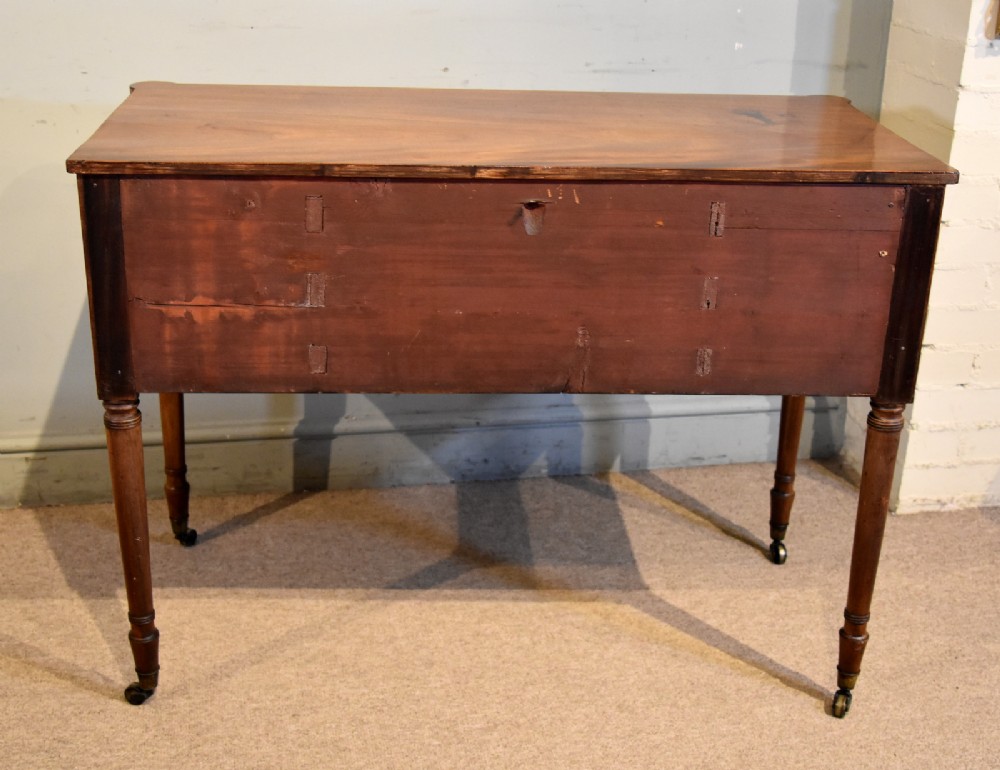 A Regency period mahogany dressing table featuring five drawers, circular brass handles, and turned tapered legs on brass castors. View VII