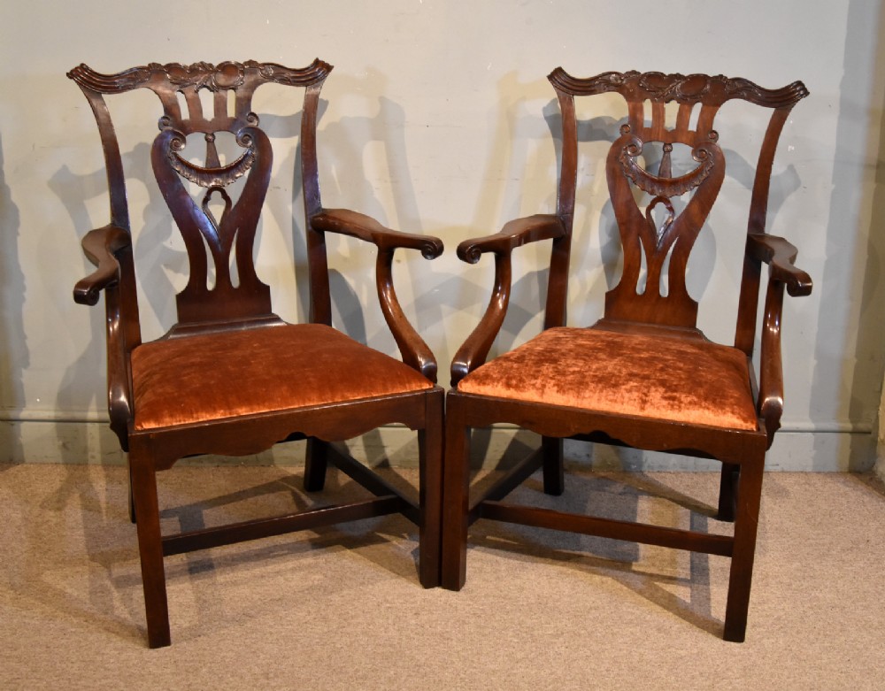 A pair of 18th-century mahogany Irish Chippendale armchairs featuring hand-carved pierced splats, curved arms, and rust-coloured velvet seat pads.