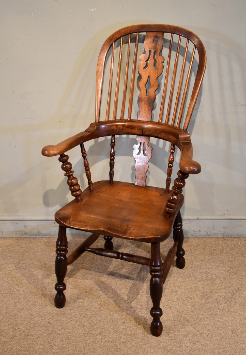 A 19th-century hoop-back Windsor armchair featuring turned wood spindles, a central pierced splat, a contoured saddle seat, and turned legs with an H-stretcher.