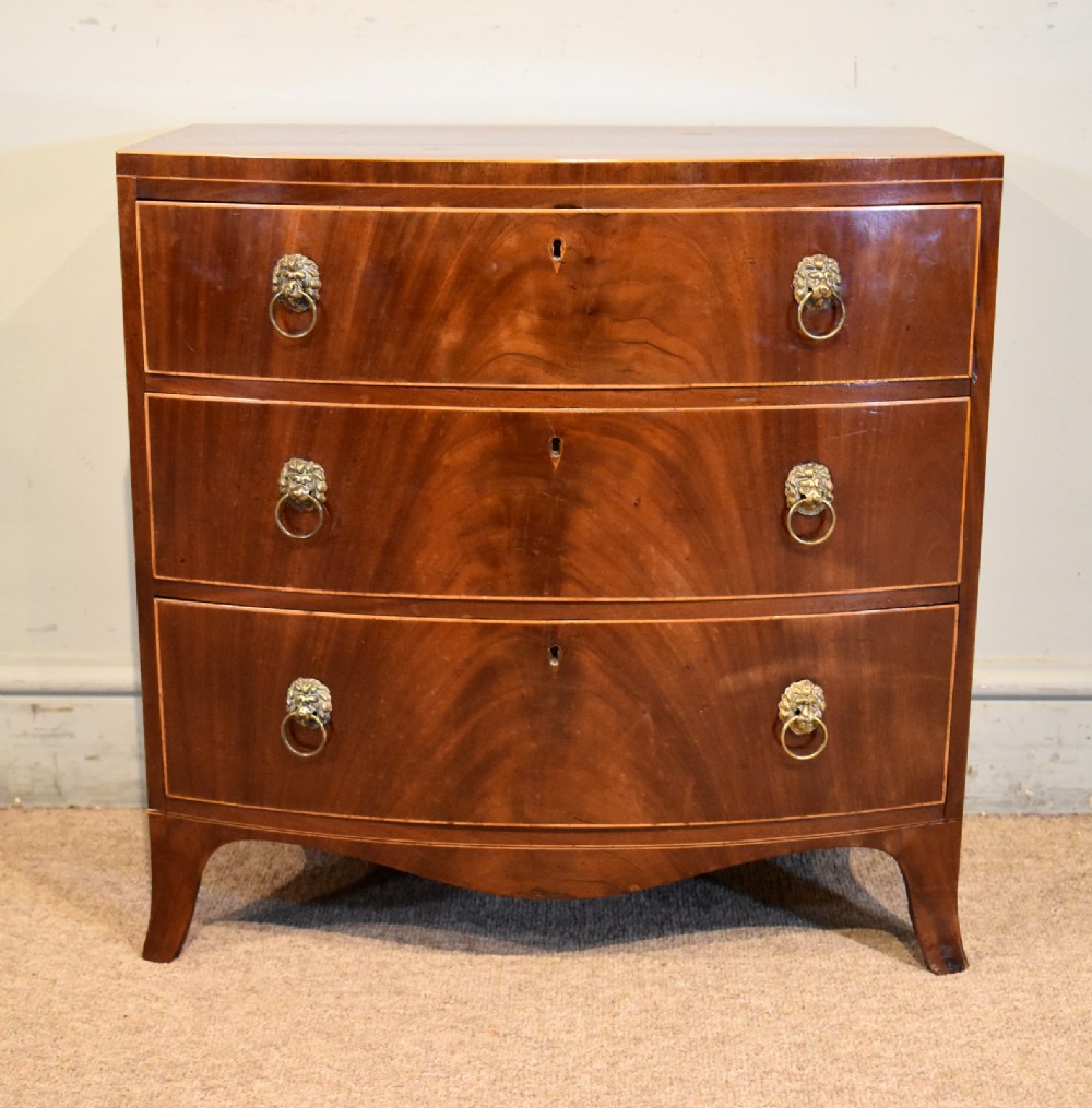 A Regency miniature bow-fronted chest of drawers made from flame mahogany with brass lion mask ring handles and boxwood stringing.