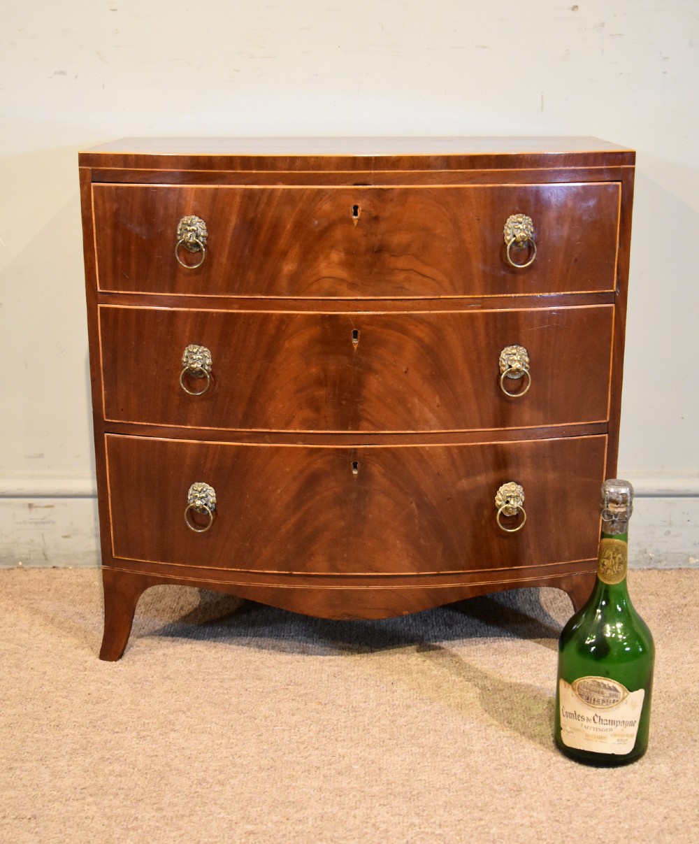 A Regency miniature bow-fronted chest of drawers made from flame mahogany with brass lion mask ring handles and boxwood stringing. View II