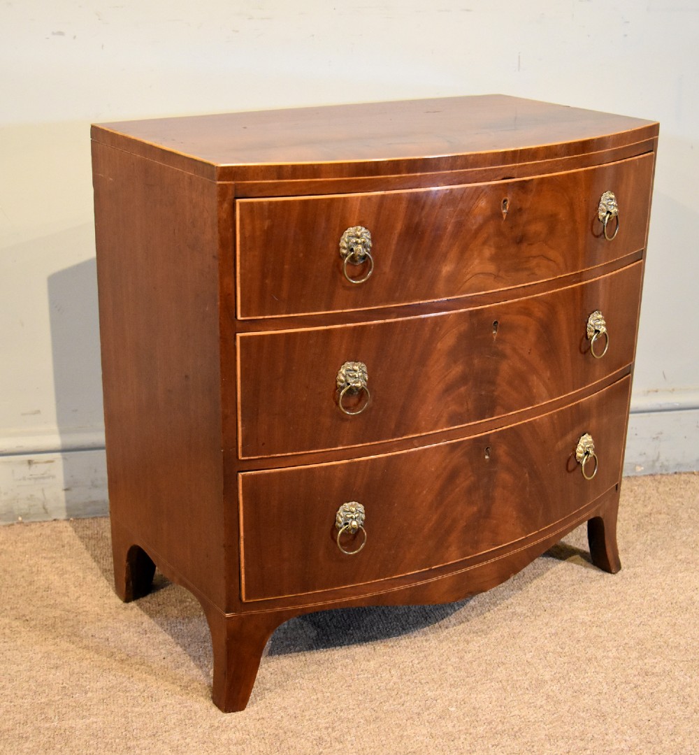 A Regency miniature bow-fronted chest of drawers made from flame mahogany with brass lion mask ring handles and boxwood stringing. View IV