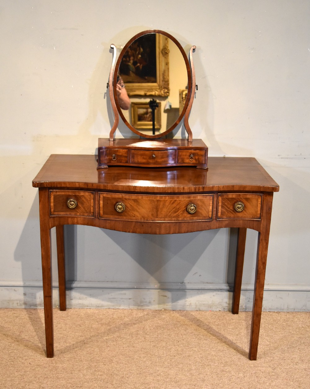 A George III mahogany dressing table featuring a serpentine front, three drawers with brass ring handles, crossbanded inlay, and four square tapered legs. View II