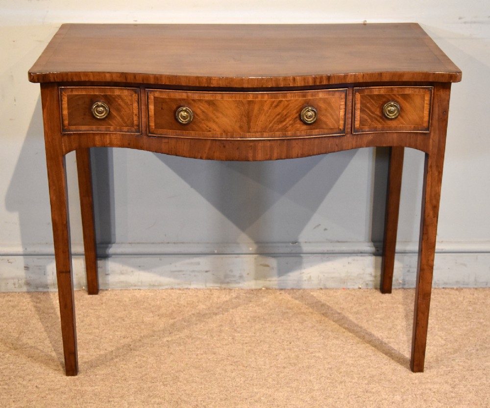 A George III mahogany dressing table featuring a serpentine front, three drawers with brass ring handles, crossbanded inlay, and four square tapered legs. View III