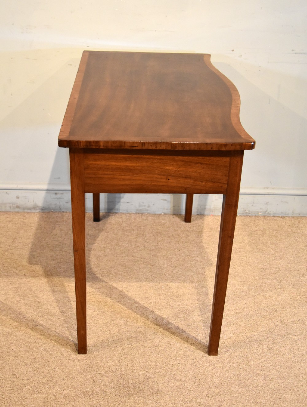 A George III mahogany dressing table featuring a serpentine front, three drawers with brass ring handles, crossbanded inlay, and four square tapered legs. View VI