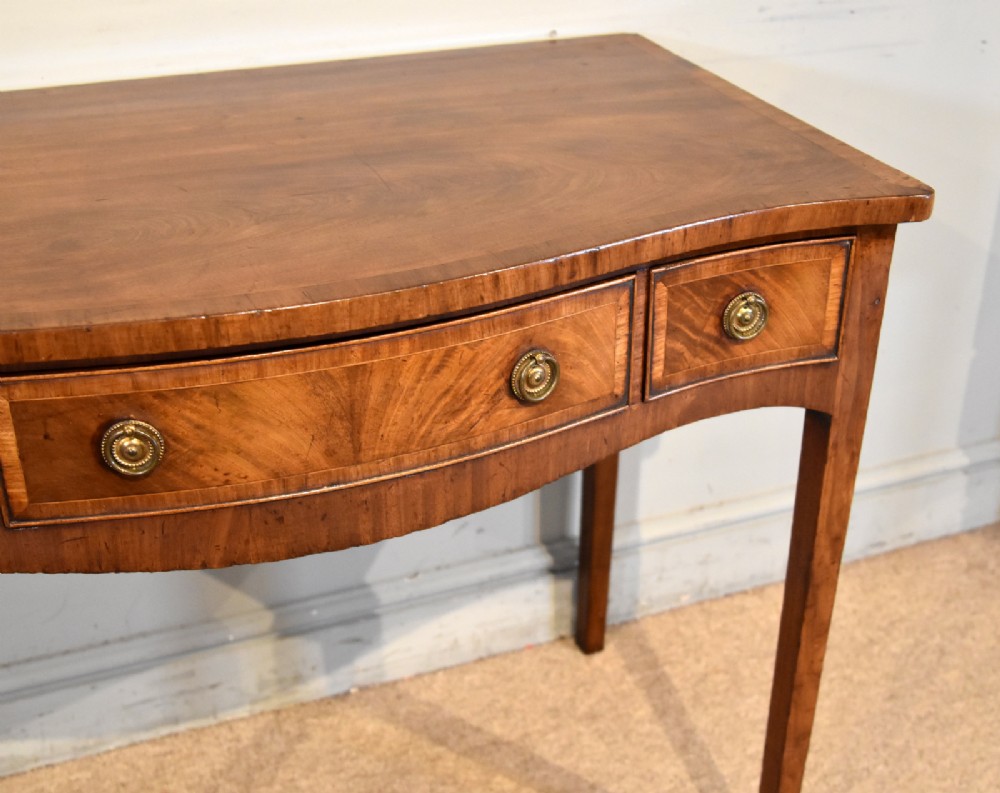 A George III mahogany dressing table featuring a serpentine front, three drawers with brass ring handles, crossbanded inlay, and four square tapered legs. View VIII