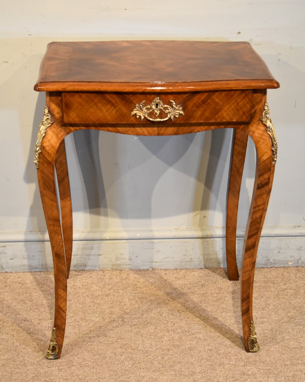 A 19th-century French walnut work table featuring curved cabriole legs, brass knee and foot mounts, a single front drawer with an ornate handle, and matched wood veneer.