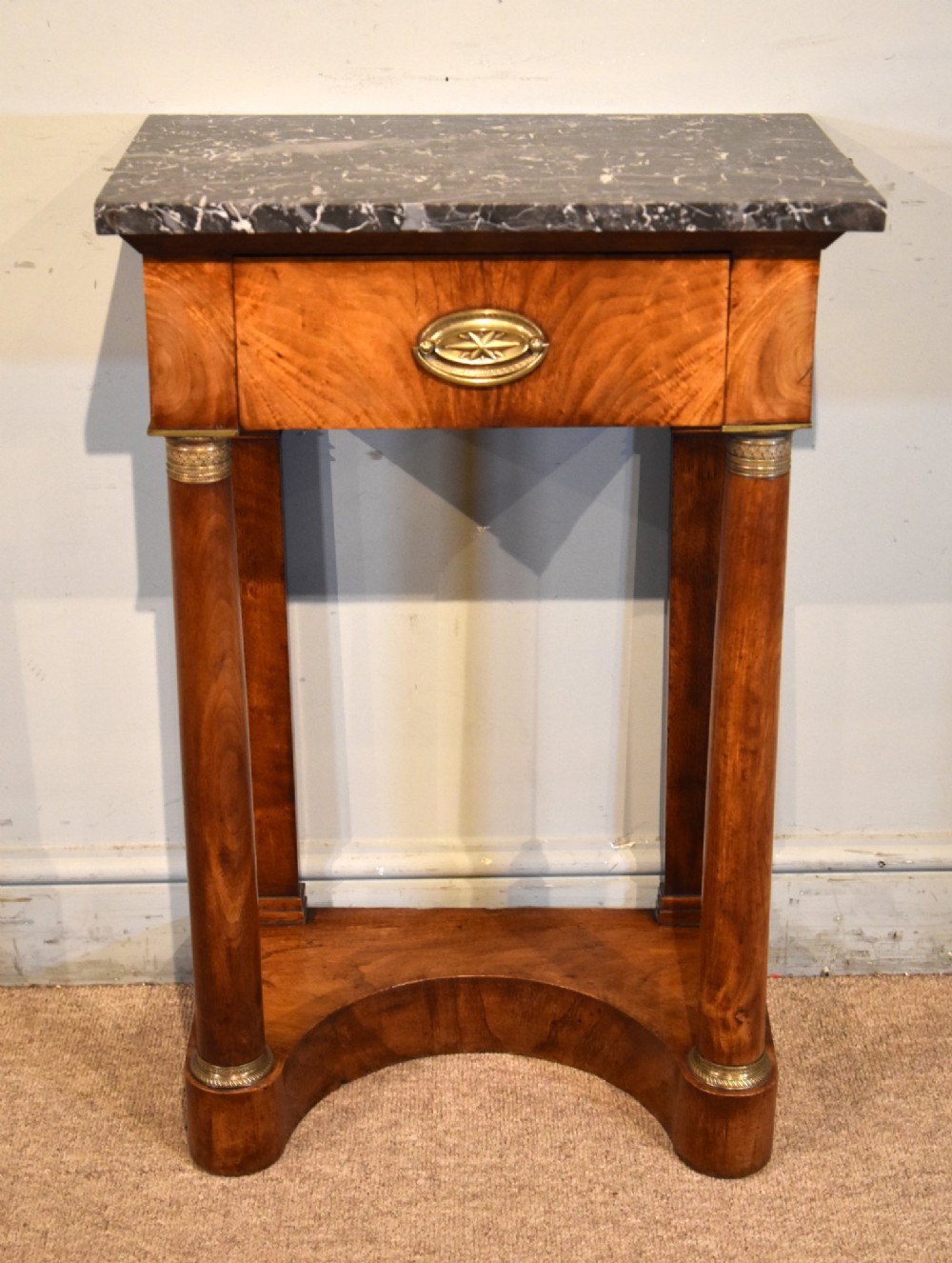 A French Empire flame mahogany console table featuring a grey speckled marble top, a single frieze drawer, and cylindrical column front legs on a shaped base.